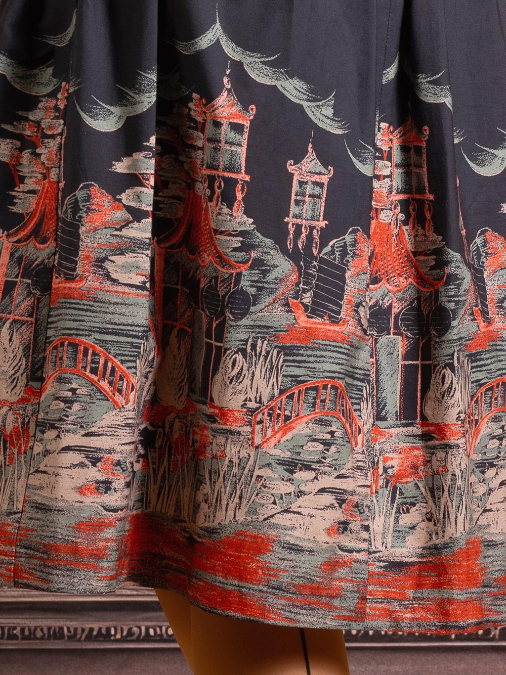 Close-up of Pagoda border print detail showing copper and sage green pagodas on black cotton fabric