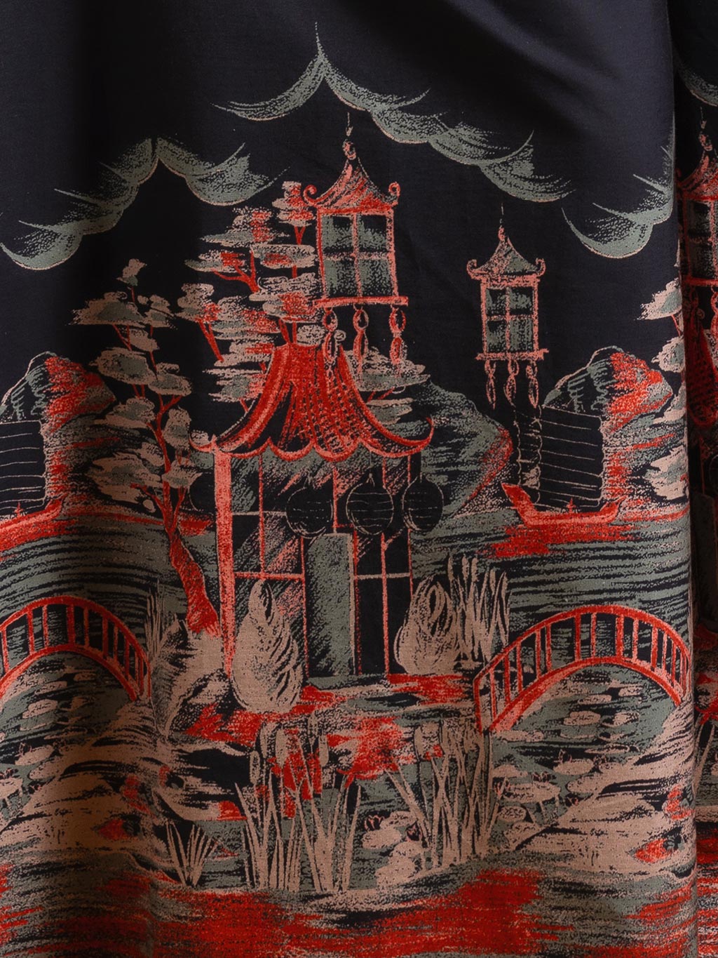 Close-up of Pagoda border print detail showing copper and sage green pagodas on black cotton fabric